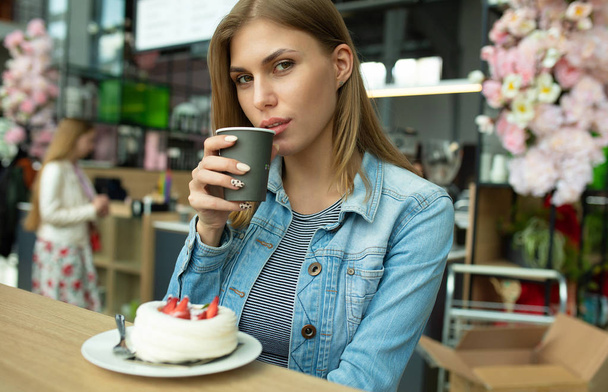 Gorgeous smiling young woman eating cake and drinking coffee at a cafeteria.  - Fotoğraf, Görsel