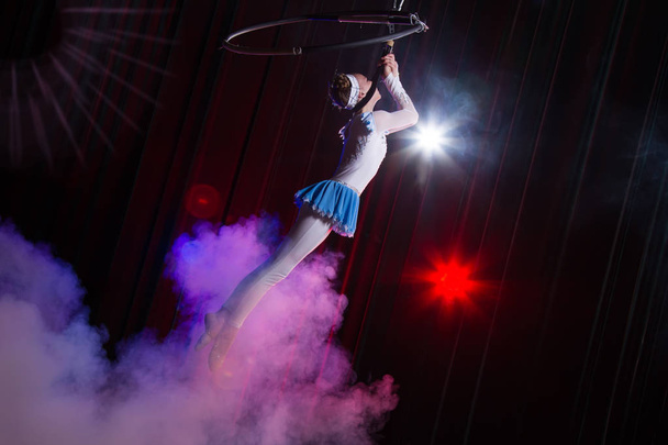 Κάνει μια κοπέλα από το τσίρκο. Ο αερογυμναστής του τσίρκου στο στεφάνι. Ακροβατικά. Έφηβος εκτελεί ένα ακροβατικό κόλπο στον αέρα - Φωτογραφία, εικόνα