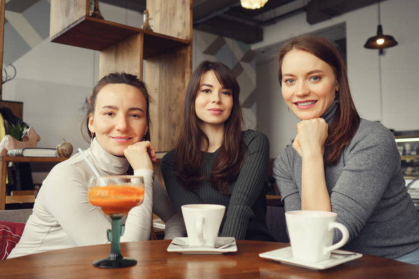 Three women girlfriends in a cafe are talking and drinking their beverages - Photo, Image