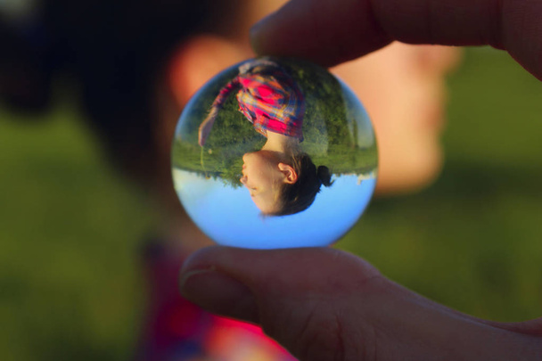 Retrato desfocado de uma jovem menina reflexão em uma bola de vidro ao ar livre. Pessoas abstratas. Pessoal, conceito de viagem. Dedos femininos segurando bola de vidro
.  - Foto, Imagem