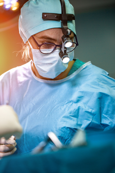 Cirujano realizando cirugía en quirófano del hospital. Cirujano en máscara con lupas durante la procadure médica
. - Foto, imagen