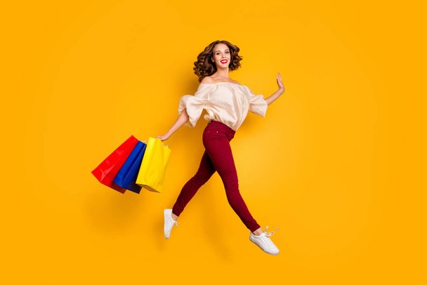 Full length body size view portrait of nice attractive pretty slim fit thin careless cheerful cheery wavy-haired lady carrying colorful bags isolated over bright vivid shine yellow background - Zdjęcie, obraz