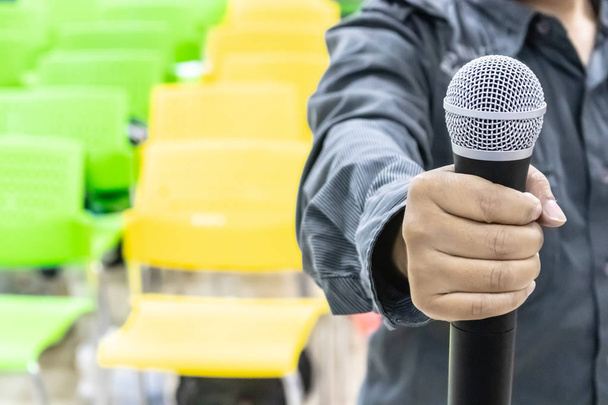 Микрофон в руке человека с разноцветными стульями
 - Фото, изображение