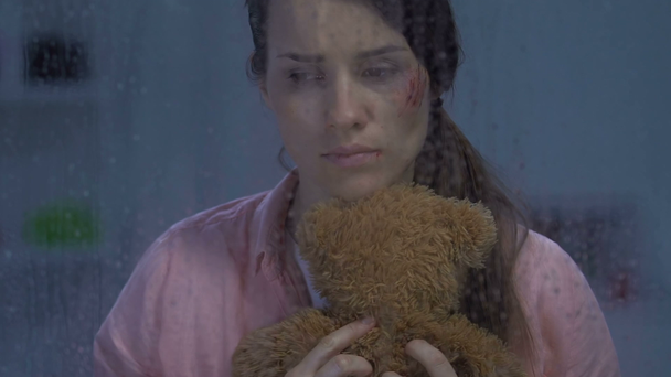 Λυπημένο θηλυκό με πληγή στο μάγουλο αγκάλιασμα αρκουδάκι, ενθυμούμενος ευτυχισμένη παιδική ηλικία - Πλάνα, βίντεο
