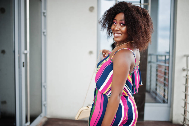 Fashionable african american woman in pink striped jumpsuit, wit - Foto, Imagen
