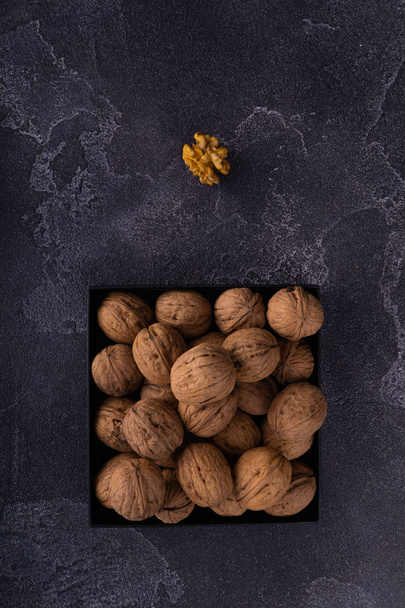 Whole and cracked walnuts on a square plate on blue textured surface, top view. Healthy nuts and seeds composition. - Foto, Bild