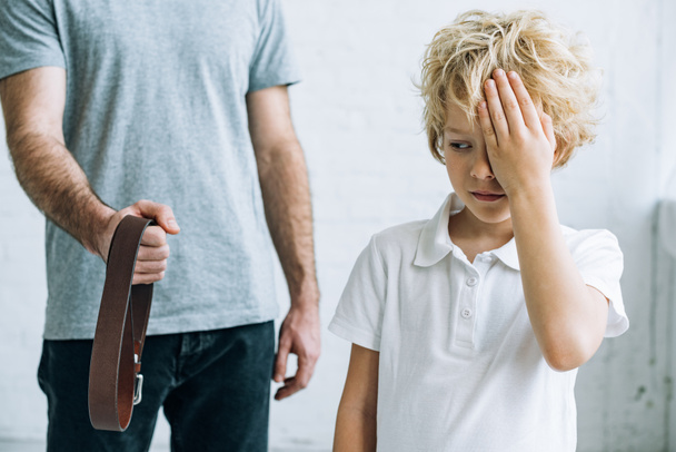 cropped view of father with belt and upset son at home - Photo, Image