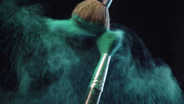 slow motion shoot of cosmetic brushes making splashes of green holi paint on black background - Footage, Video