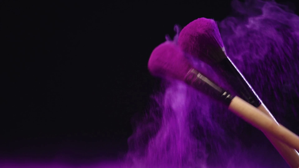 slow motion shoot of cosmetic brushes hitting and making splashes of colorful purple holi paint on black background - Footage, Video