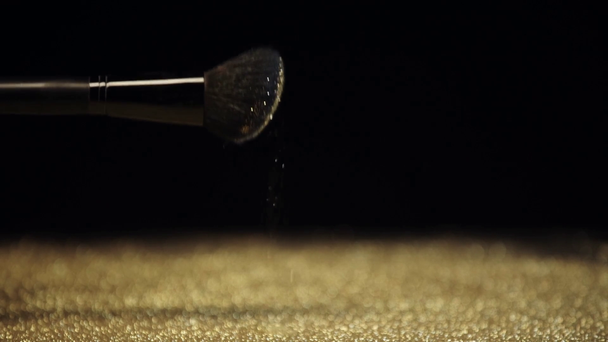 slow motion shoot of cosmetic brush shaking and scattering bright golden glitter - Séquence, vidéo