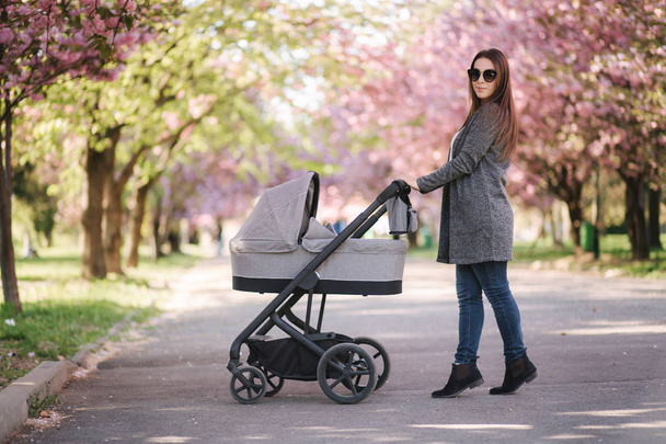 Happy mom walk with her little baby girl in stroller. Background of pink sakura tree - Foto, immagini