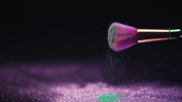 slow motion shoot of cosmetic brush shaking and scattering shiny purple and green sparkles - Footage, Video