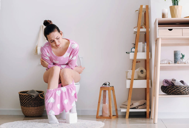 Молодая женщина страдает диареей на унитазе дома
 - Фото, изображение
