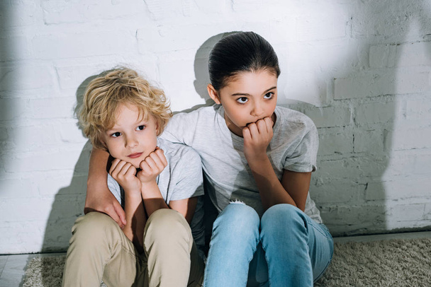 scared sister embracing brother while sitting on carpet - Photo, Image