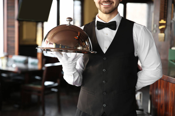 Fiatal férfi pincér tálca és cloche étteremben - Fotó, kép
