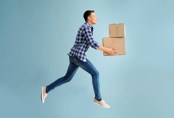 Jumping young man with boxes on grey background - Photo, Image