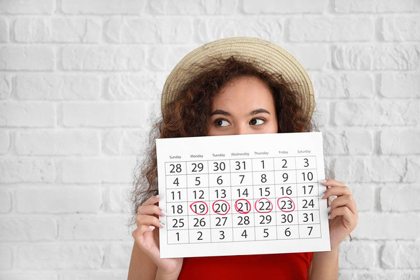 Femme afro-américaine tenant un calendrier avec des jours marqués de menstruation sur fond blanc
 - Photo, image