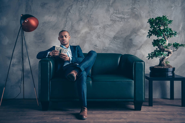 Portrait of nice classy chic elegant attractive content busy guy wearing jacket suit executive manager masculine sitting on couch account sum budget at workplace station gray concrete wall - Fotografie, Obrázek