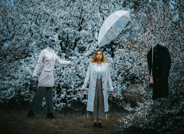 Een vrouw staat in een bloeiende tuin tussen mannequins en een umbr - Foto, afbeelding