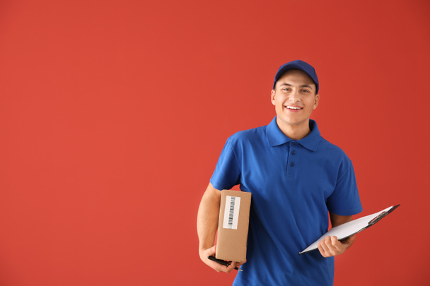 Delivery man with box and clipboard on color background - Photo, Image