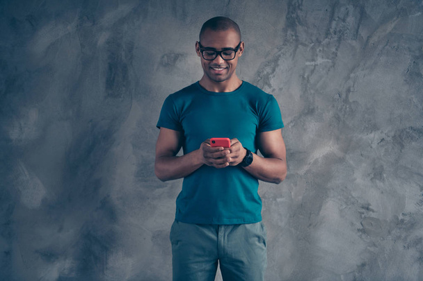 Portrait of his he nice lovely cute attractive good-looking cheerful cheery well-groomed masculine guy wearing blue t-shirt using new device gadget isolated over gray industrial concrete wall - Fotoğraf, Görsel