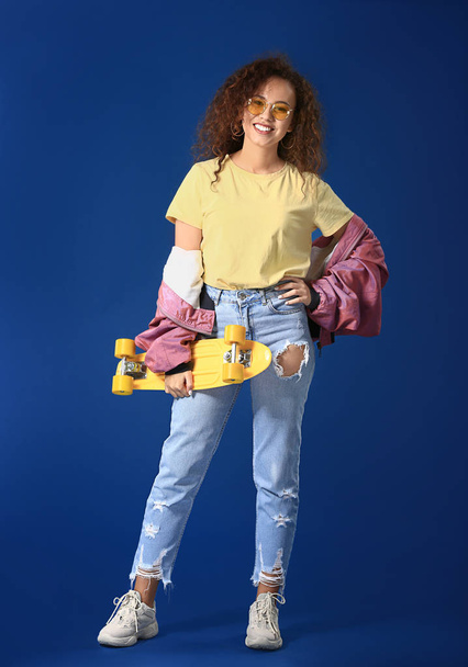 stilvolle junge Frau mit Skateboard auf farbigem Hintergrund - Foto, Bild