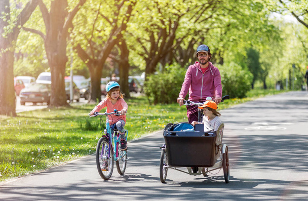 Padre e hijas teniendo un paseo con bicicleta de carga durante la primavera
 - Foto, Imagen