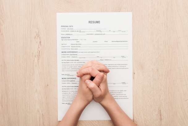partial view of recruiter holding clenched hands on resume template on wooden table - Photo, Image