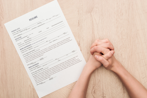 cropped view of recruiter holding clenched hands near resume template on wooden table - Фото, изображение