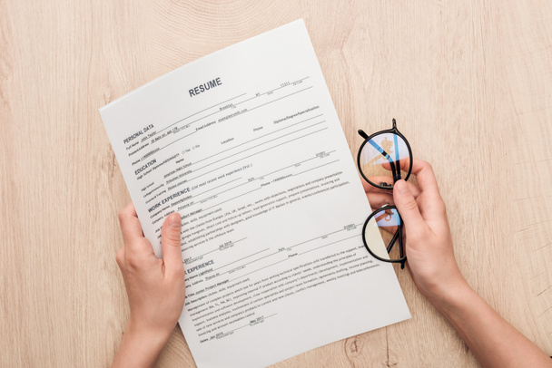 partial view of recruiter holding resume template and glasses on wooden table - Foto, Imagen