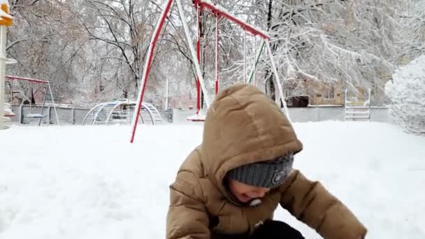4k video of happy smiling toddler boy throwing snowballs on playground at winter park after snow storm - Footage, Video