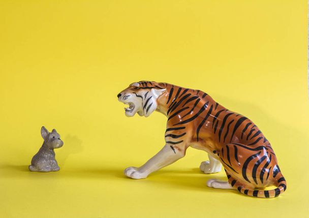 Tiger and small dog on a yellow background. Porcelain figurine. Dog breed terrier. Amur tiger. - Photo, Image