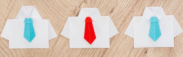 panoramic shot of origami white shirts with blue ties with one red on wooden background - Foto, Imagem