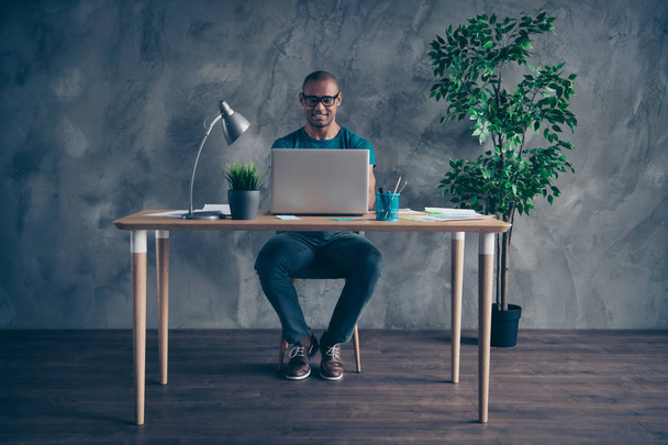 Full length body size photo amazing he him his macho handsome notebook table lamp light green plant reliable person excited duty wear specs blue t-shirt pants sit chair indoors workstation office - Foto, Imagen