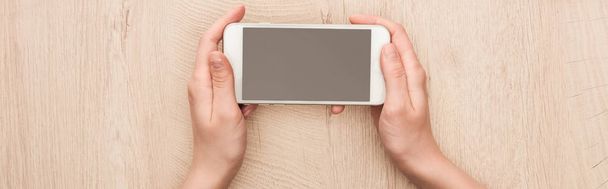 panoramic shot of woman holding smartphone with blank screen at wooden table - Foto, Imagem