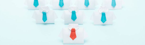 panoramic shot of origami white shirts with blue ties with one red on blue background, leadership concept - Foto, Imagem