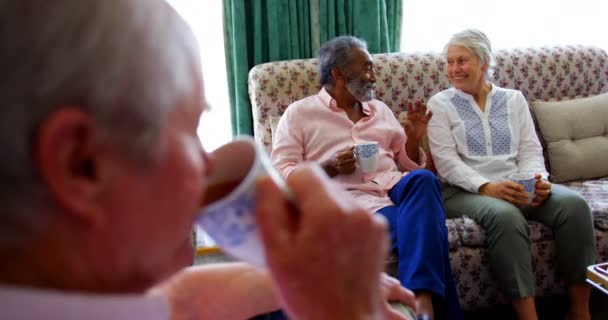 Close-up of active Caucasian senior man drinking coffee at nursing home . Senior friends interacting with each other in the background  - Záběry, video