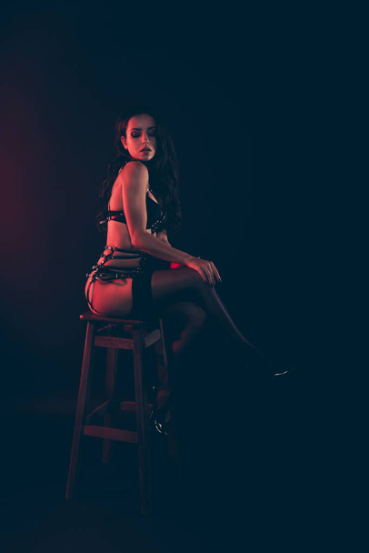 Vertical of nice lovely magnificent delicate attractive fit thin wavy-haired lady wearing swordbelt sitting on chair bar stool isolated over red light black background - Foto, Imagen