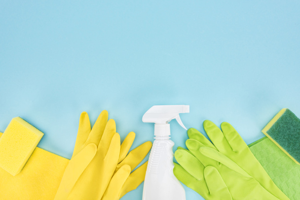 top view of yellow and green rubber gloves, sponges, rags and spray bottle with detergent on blue background with copy space - Fotoğraf, Görsel