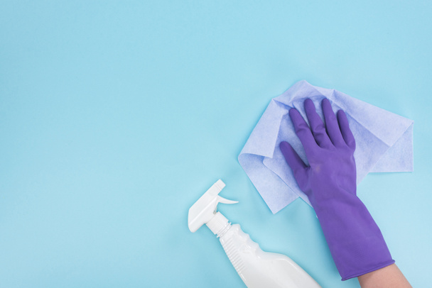 vista cortada de limpador em luva de borracha roxa segurando pano perto de frasco de spray com detergente no fundo azul
 - Foto, Imagem