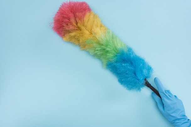 cropped view of cleaner in rubber glove holding rainbow duster on blue background - Фото, зображення