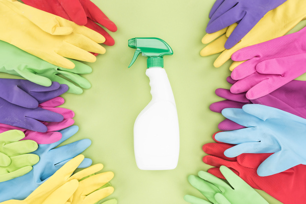 yeşil arka plan üzerinde deterjan ile sprey şişesi etrafında çok renkli kauçuk eldiven üst görünümü - Fotoğraf, Görsel