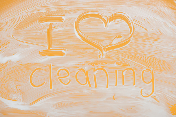 i love cleaning handwritten lettering written on glass with white foam on orange background - Photo, Image