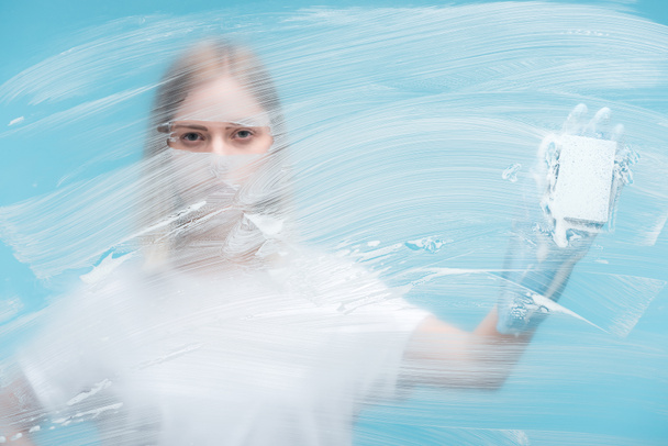 επιλεκτική εστίαση των γυναικών μάτια κοιτάζοντας μέσα από γυαλί με λευκό αφρό σε μπλε φόντο - Φωτογραφία, εικόνα