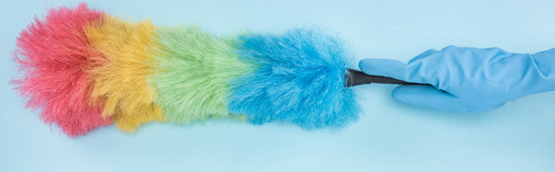 panoramic shot of cleaner in rubber glove holding rainbow duster on blue background - Photo, Image