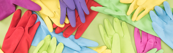 panoramische foto van verspreide veelkleurige rubberen handschoenen op groene achtergrond - Foto, afbeelding