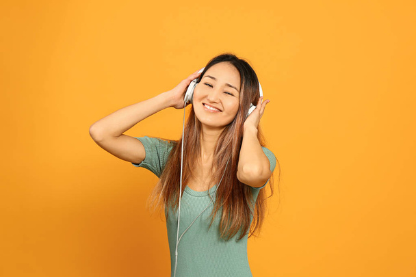 Aziatische vrouw luisteren naar muziek op kleur achtergrond - Foto, afbeelding