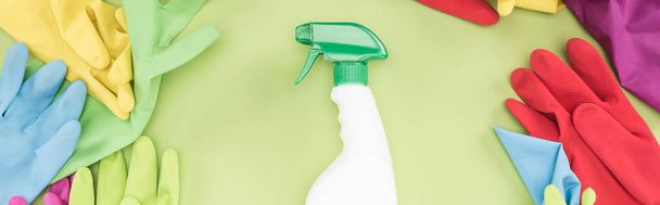 Panoramaaufnahme von Gummihandschuhen im Kreis um Sprühflasche mit Waschmittel auf grünem Hintergrund - Foto, Bild