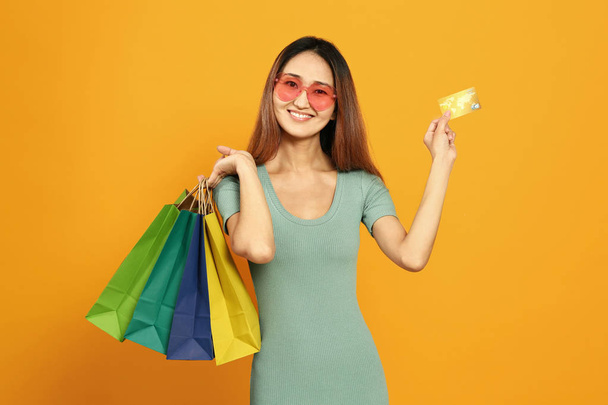 Donna asiatica con borse della spesa e carta di credito su sfondo a colori
 - Foto, immagini