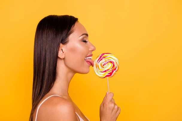 Close up side profile photo beautiful she her lady hungry addicted sweets person big lolly pop wooden stick licking overjoyed eyes closed wear casual pastel tank-top isolated yellow bright background - Фото, зображення